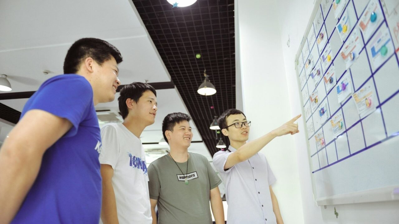 Four men gathered around a whiteboard with sticky notes.