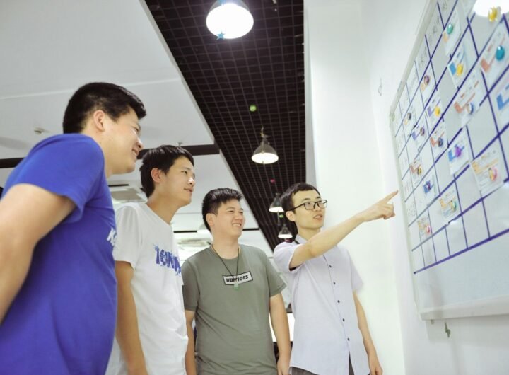 Four men gathered around a whiteboard with sticky notes.