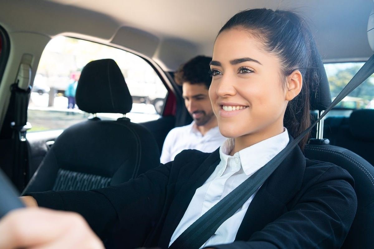 Une conductrice souriante au volant, passager à l'arrière, ceinture attachée