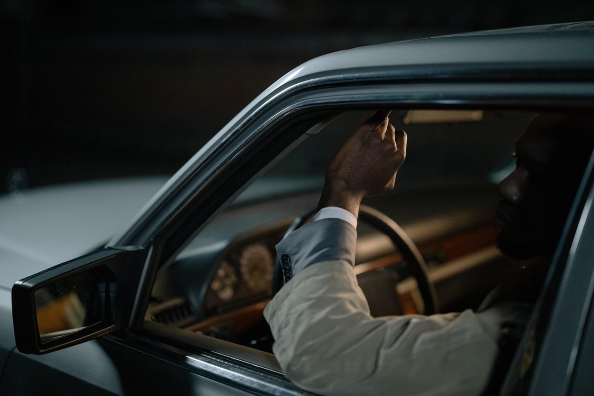 Homme assis dans une voiture, main sur le volant, regardant à l'extérieur Homme assis dans une voiture, main sur le volant, regardant à l'extérieur
