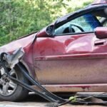 Voiture rouge avec dommage au pare-chocs et au pneu, sur une route entourée de verdure