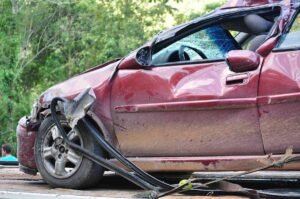 Voiture rouge avec dommage au pare-chocs et au pneu, sur une route entourée de verdure