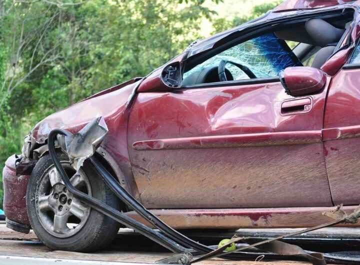 Voiture rouge avec dommage au pare-chocs et au pneu, sur une route entourée de verdure