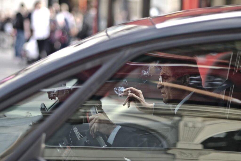 Un homme dans une voiture, main levée, reflet de la rue