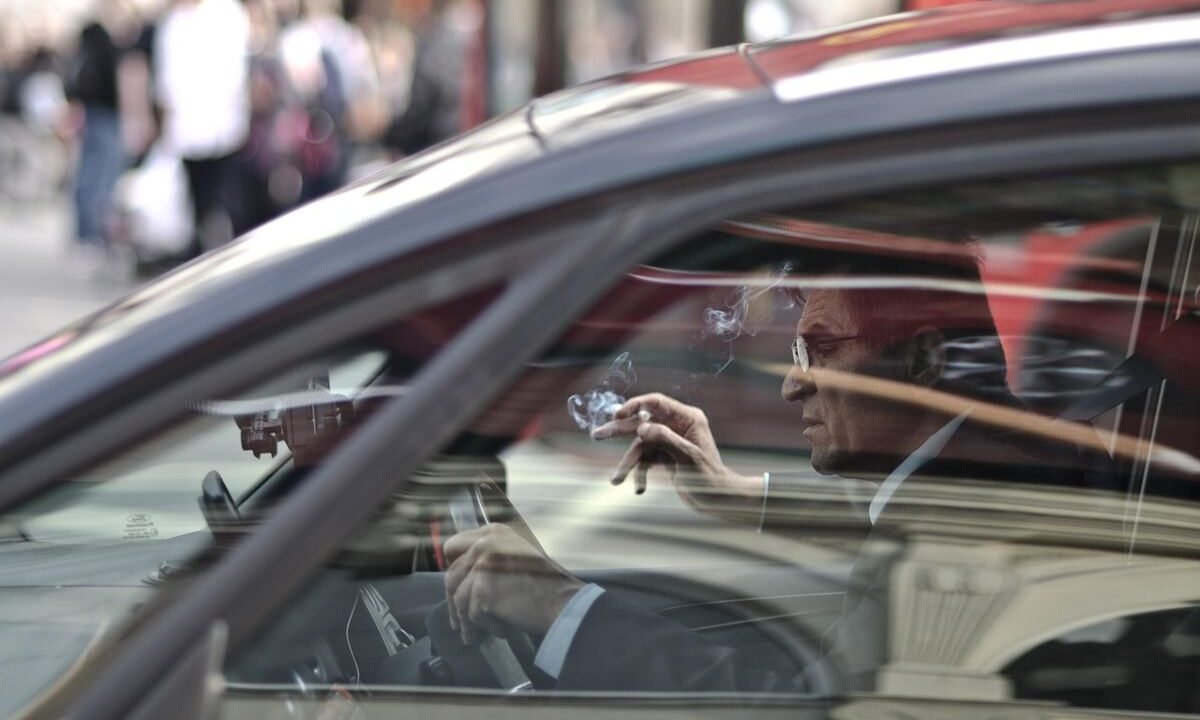 Un homme dans une voiture, main levée, reflet de la rue