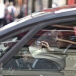 Un homme dans une voiture, main levée, reflet de la rue