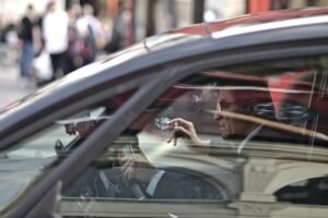 Un homme dans une voiture, main levée, reflet de la rue