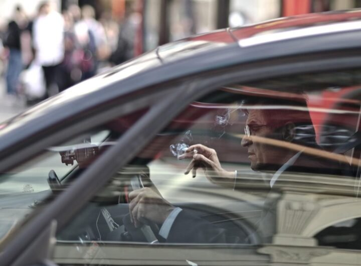 Un homme dans une voiture, main levée, reflet de la rue