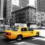 Taxi jaune circulant dans une avenue urbaine avec buildings en arrière-plan, scène de rue new-yorkaise