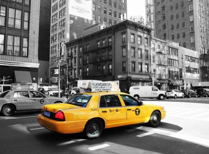 Taxi jaune circulant dans une avenue urbaine avec buildings en arrière-plan, scène de rue new-yorkaise