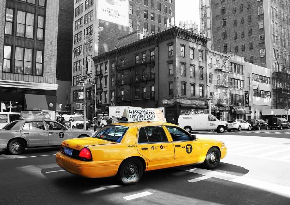 Taxi jaune circulant dans une avenue urbaine avec buildings en arrière-plan, scène de rue new-yorkaise