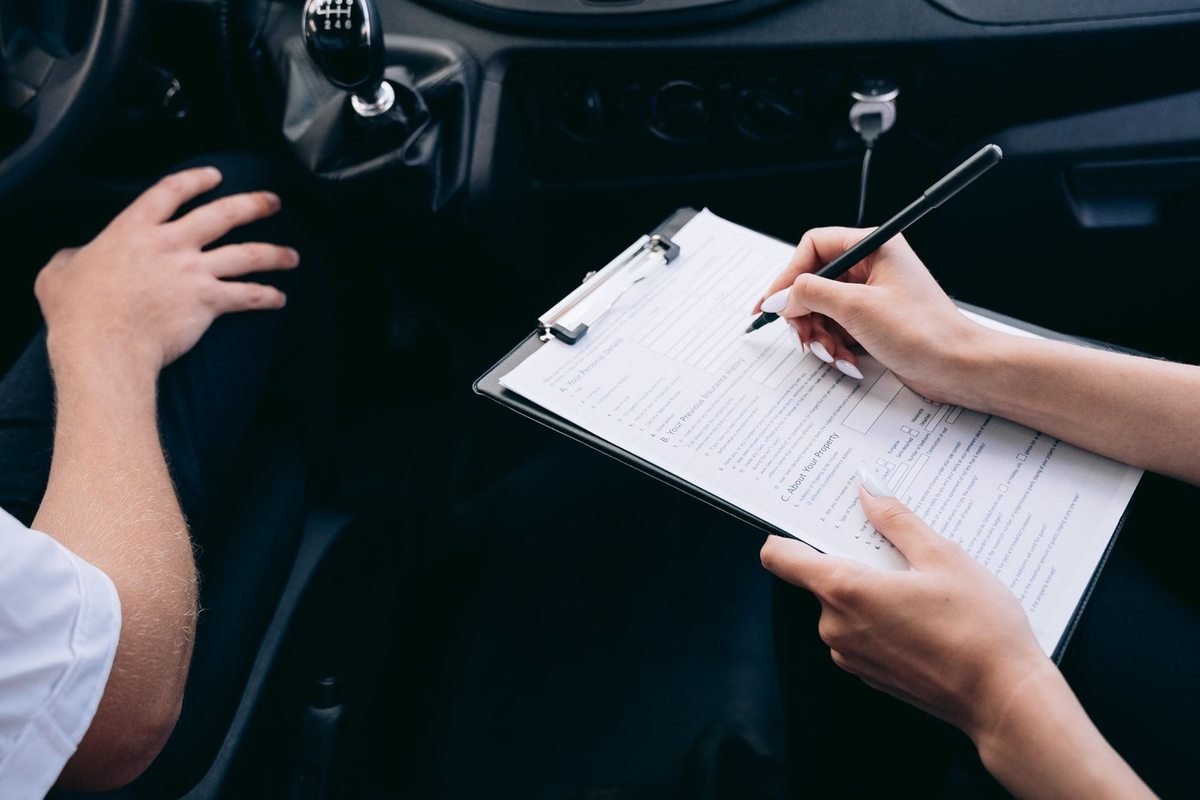 Une main écrit sur un carnet, l'autre repose sur le tableau de bord d'une voiture