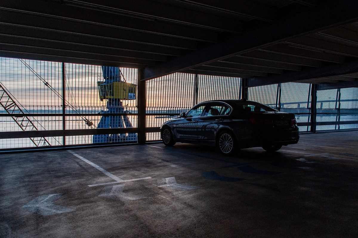 Voiture dans un parking souterrain, devant une fenêtre donnant sur un grue et un ciel coloré