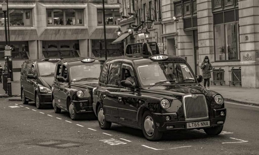 Des taxis noirs en rangée sur une rue de ville, piéton à droite