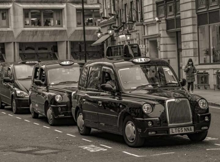 Des taxis noirs en rangée sur une rue de ville, piéton à droite