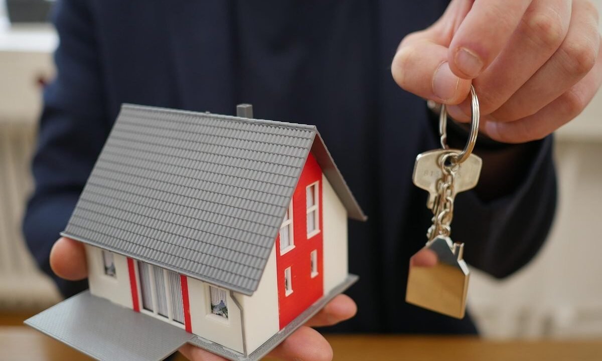 Une main tient une petite maison modèle et une clé sur une table
