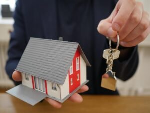 Une main tient une petite maison modèle et une clé sur une table