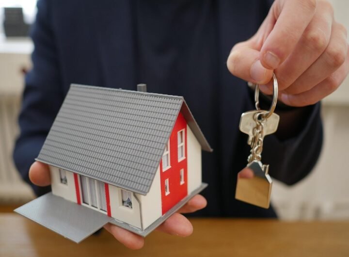 Une main tient une petite maison modèle et une clé sur une table