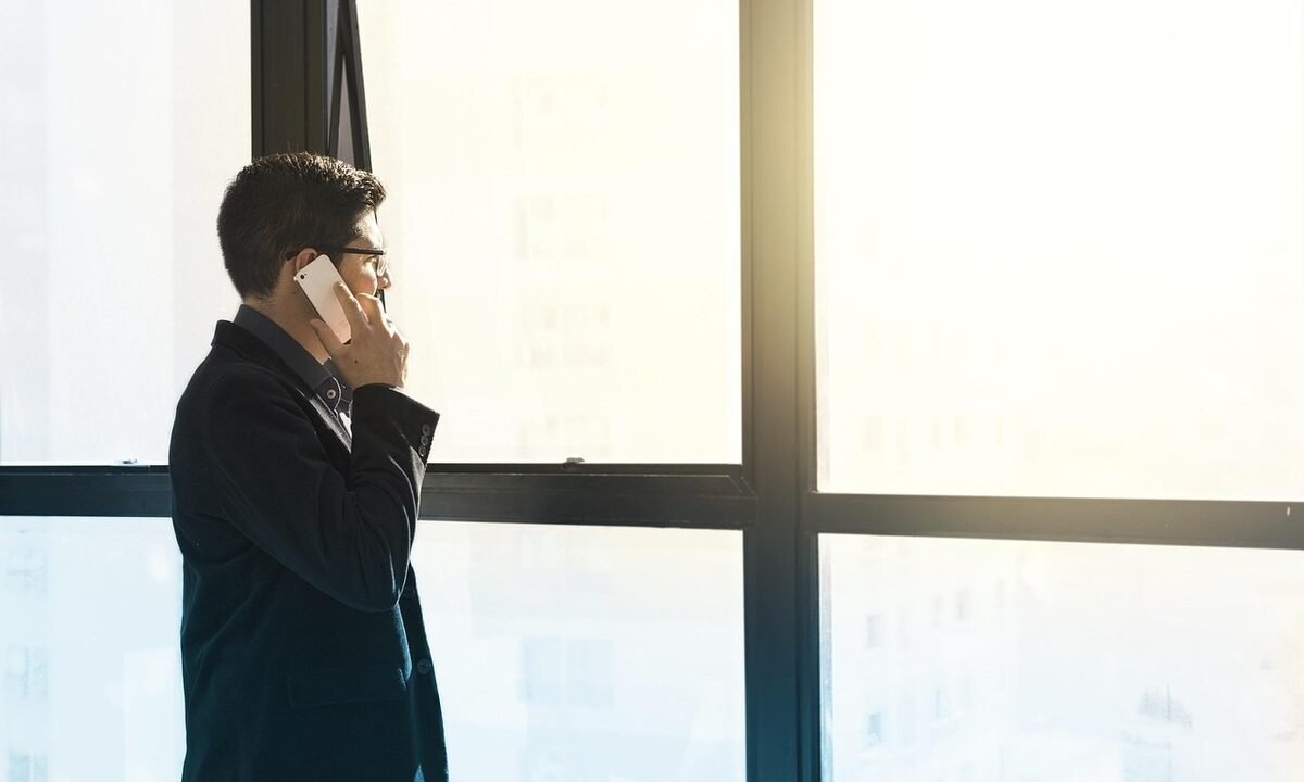 Homme en costume noir parlant au téléphone près d'une grande fenêtre