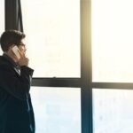 Homme en costume noir parlant au téléphone près d'une grande fenêtre