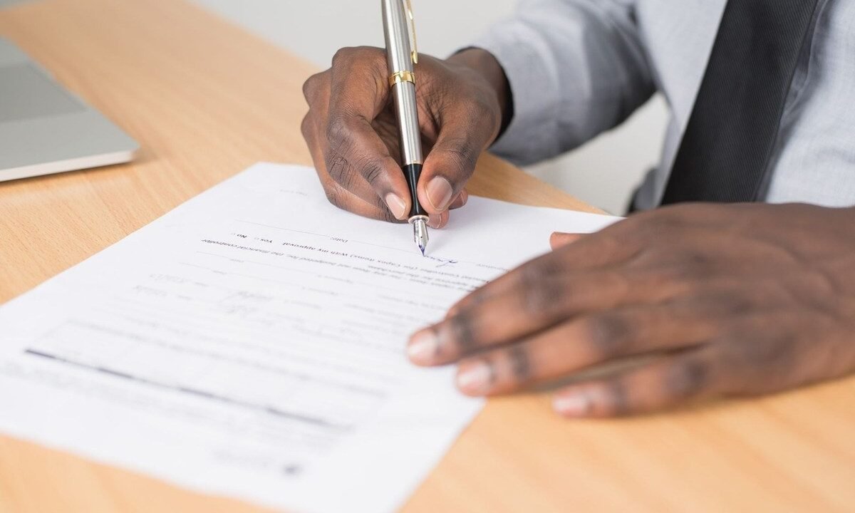 Main écrivant sur document avec stylo sur un bureau en bois