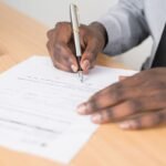 Main écrivant sur document avec stylo sur un bureau en bois