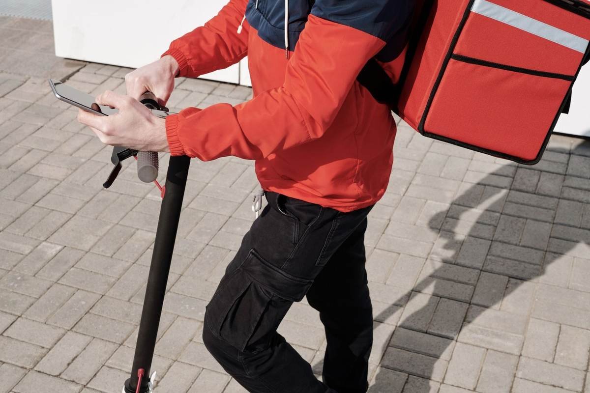 Personne sur trottinette avec téléphone et sac orange, sur trottoir
