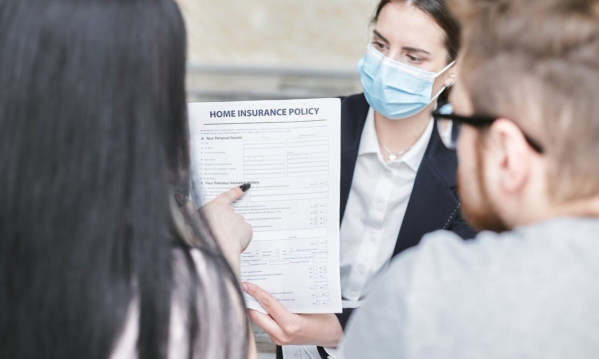 Une femme en masque montre un document d'assurance à deux clients