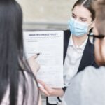 Une femme en masque montre un document d'assurance à deux clients