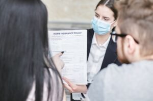 Une femme en masque montre un document d'assurance à deux clients