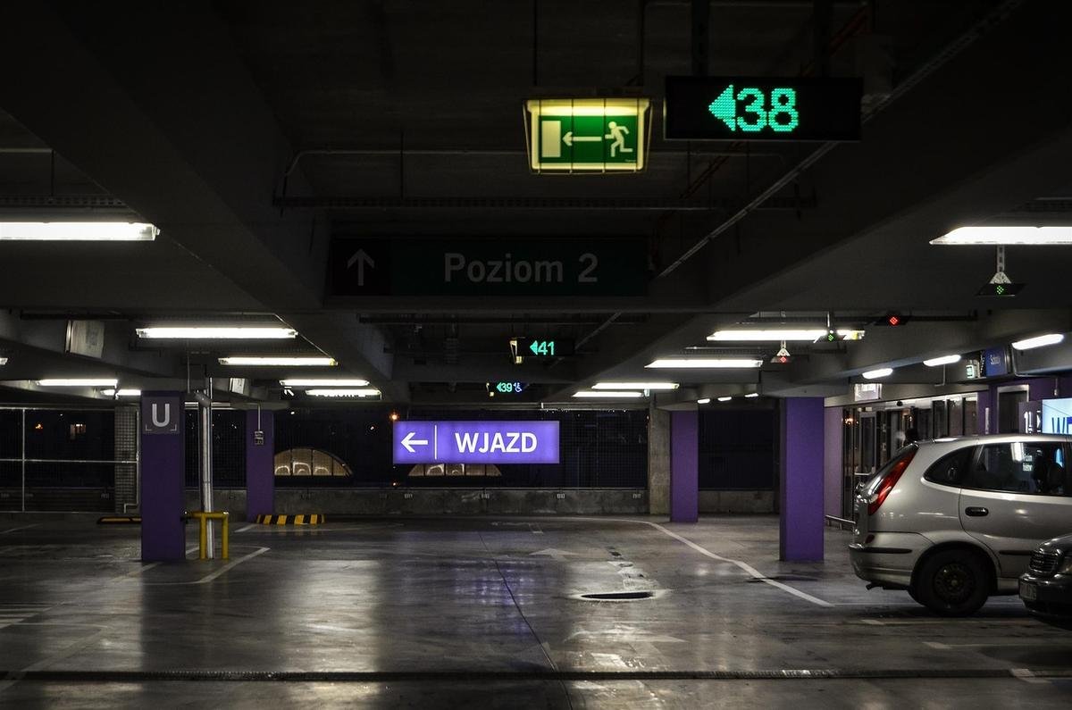 Vue d'un parking souterrain avec panneaux, colonnes violettes et véhicule Vue d'un parking souterrain avec panneaux, colonnes violettes et véhicule