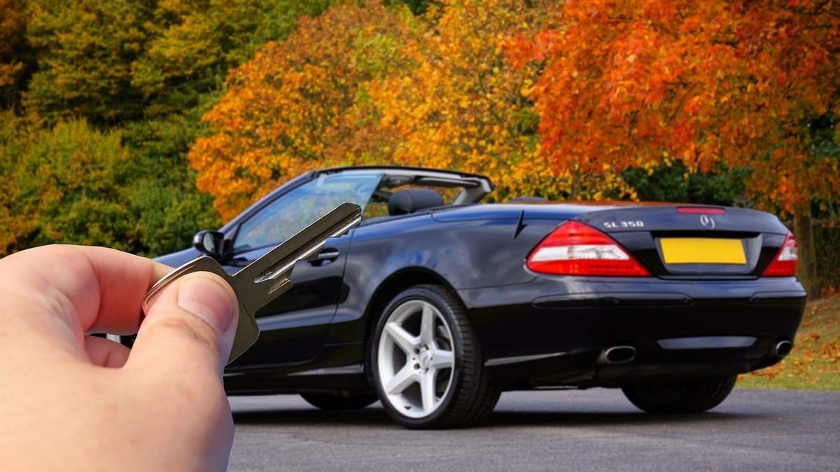 Une main tenant des clés devant une berline cabriolet noire sur route