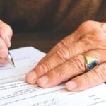 Mains âgées écrivant sur un document avec un stylo bleu sur une table en bois