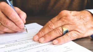 Mains âgées écrivant sur un document avec un stylo bleu sur une table en bois