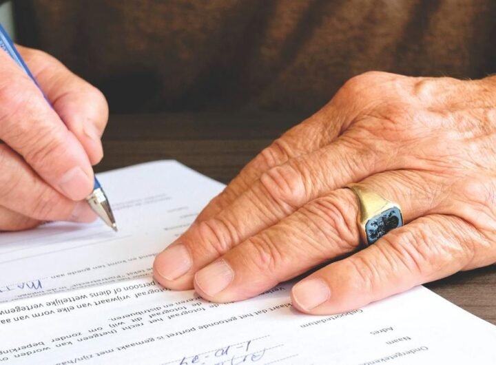 Mains âgées écrivant sur un document avec un stylo bleu sur une table en bois